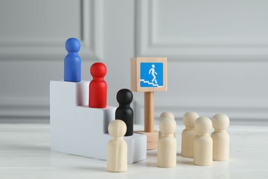 Stairs with group of different wooden human figures and road sign on white table