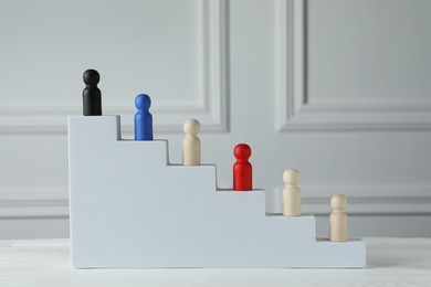 Photo of Stairs with group of different wooden human figures on white table