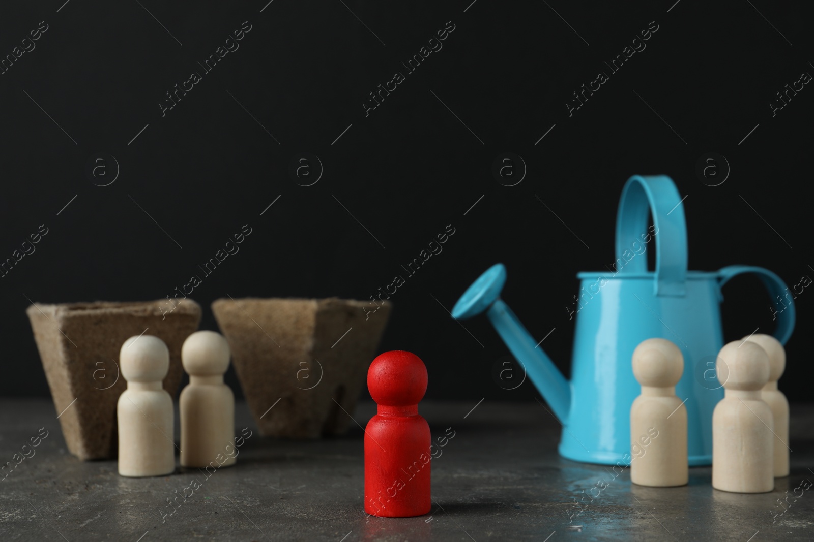 Photo of Different human figures, watering can and soil on grey textured table against dark background