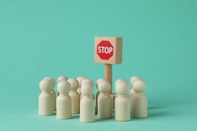 Photo of Road Stop sign blocking way for wooden human figures on turquoise background