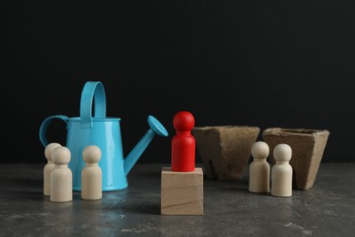 Photo of Different human figures, watering can and soil on grey textured table against dark background