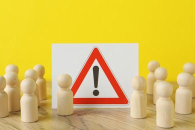 Photo of Wooden human figures among warning road sign on table against yellow background