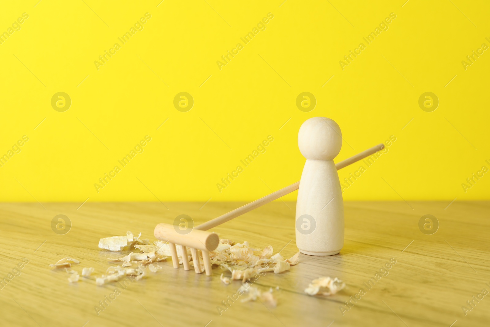 Photo of Wooden human figure with rake and sawdust on table against yellow background