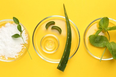 Photo of Petri dishes with green leaves and cosmetic products on yellow background, flat lay