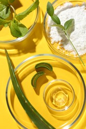 Petri dishes with green leaves and cosmetic products on yellow background, flat lay