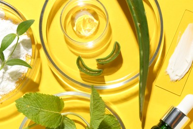 Photo of Petri dishes with green leaves and cosmetic products on yellow background, flat lay