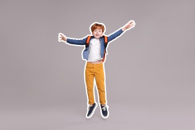 Happy school child with backpack jumping on grey background