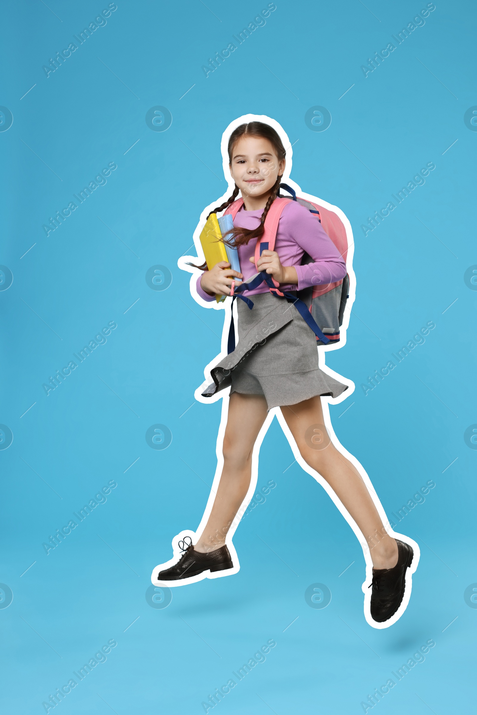 Image of School child holding books and jumping on light blue background