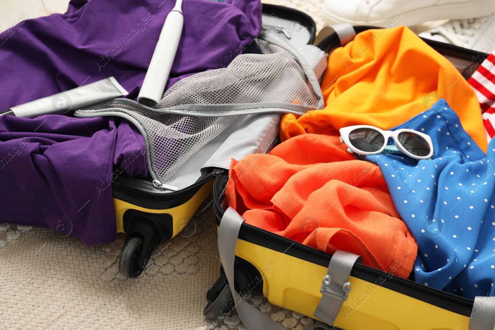 Photo of Open suitcase with traveler's belongings on floor, closeup