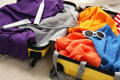 Open suitcase with traveler's belongings on floor, closeup