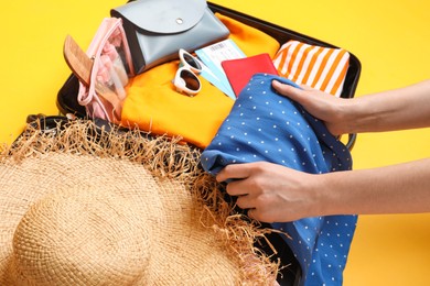 Woman packing suitcase for trip on yellow background, closeup