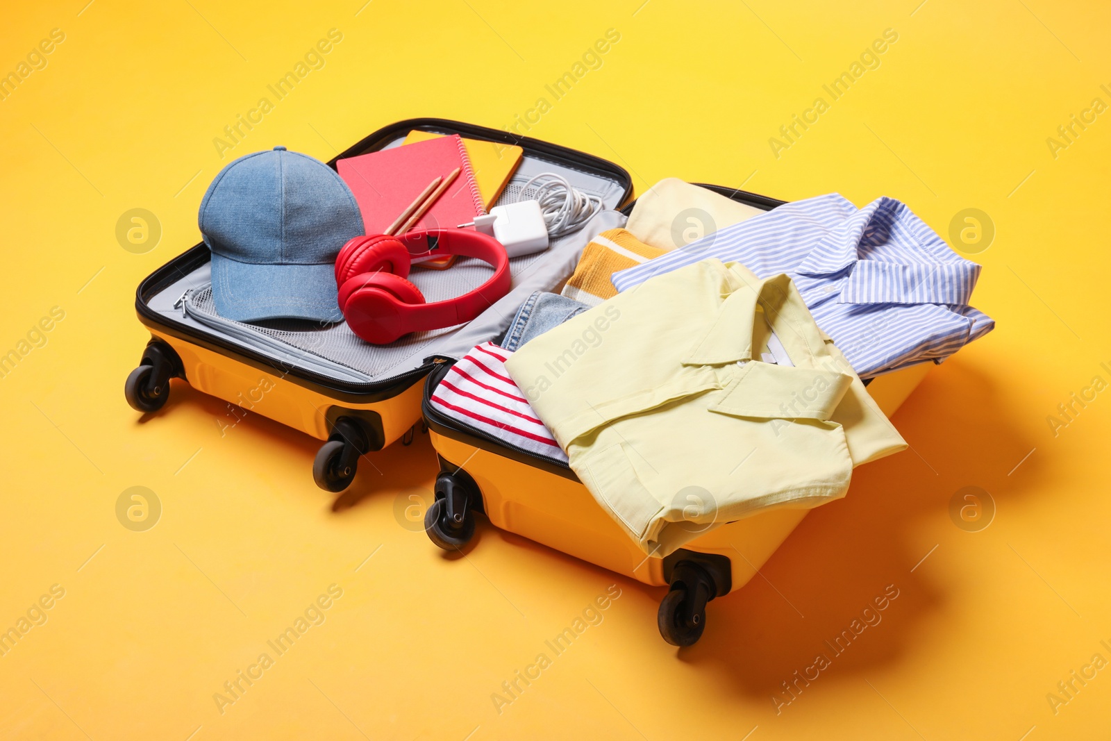 Photo of Open suitcase with traveler's belongings on yellow background