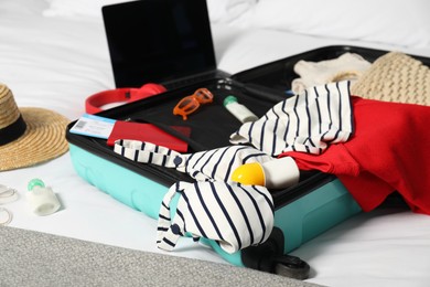 Open suitcase with traveler's belongings on bed, closeup