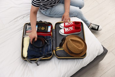 Photo of Man packing suitcase for trip on bed indoors, closeup