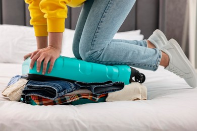 Photo of Woman packing suitcase for trip on bed indoors, closeup