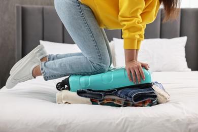 Photo of Woman packing suitcase for trip on bed indoors, closeup