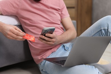 Photo of Online banking. Man with credit card, smartphone and laptop paying purchase at home, closeup