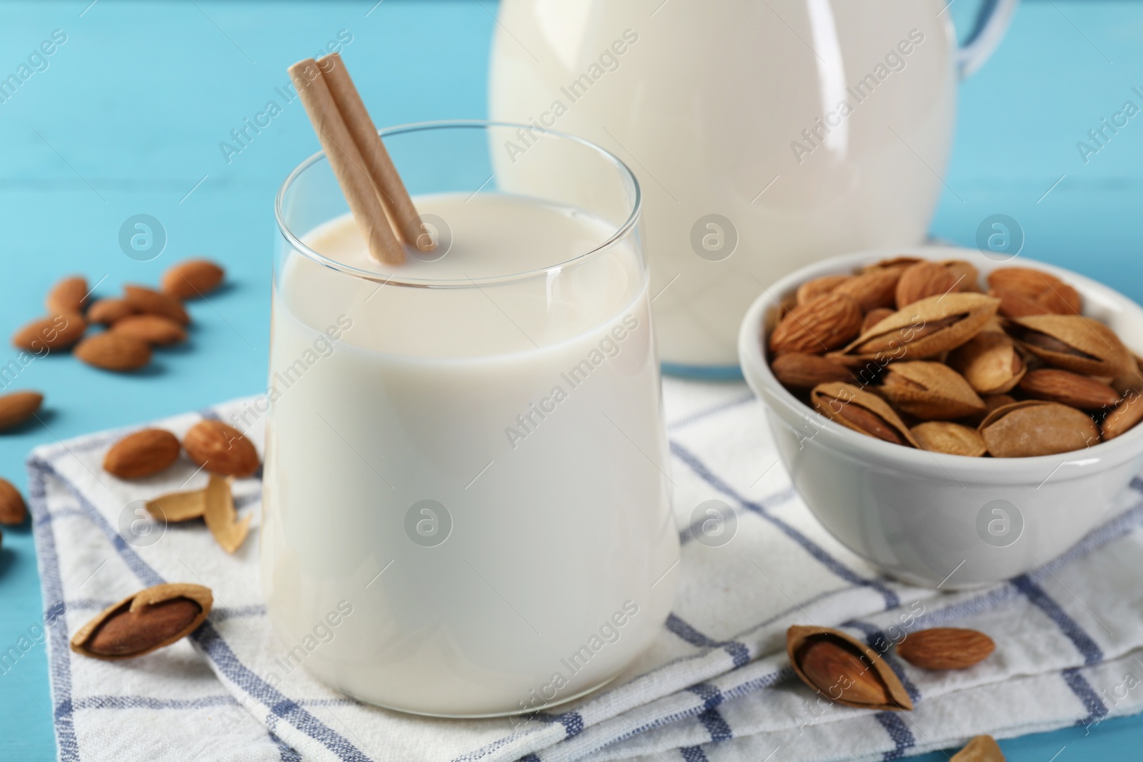 Photo of Glass of almond milk, jug and almonds on light blue wooden table, closeup