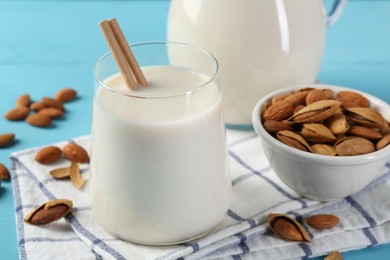 Glass of almond milk, jug and almonds on light blue wooden table, closeup