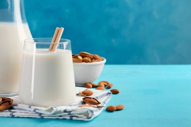 Glass of almond milk, jug and almonds on light blue wooden table, space for text