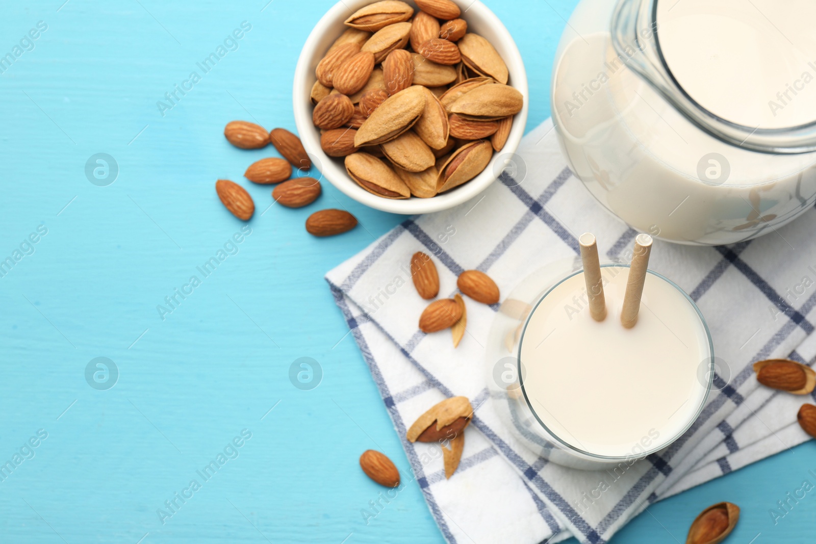 Photo of Glass of almond milk, jug and almonds on light blue wooden table, top view. Space for text