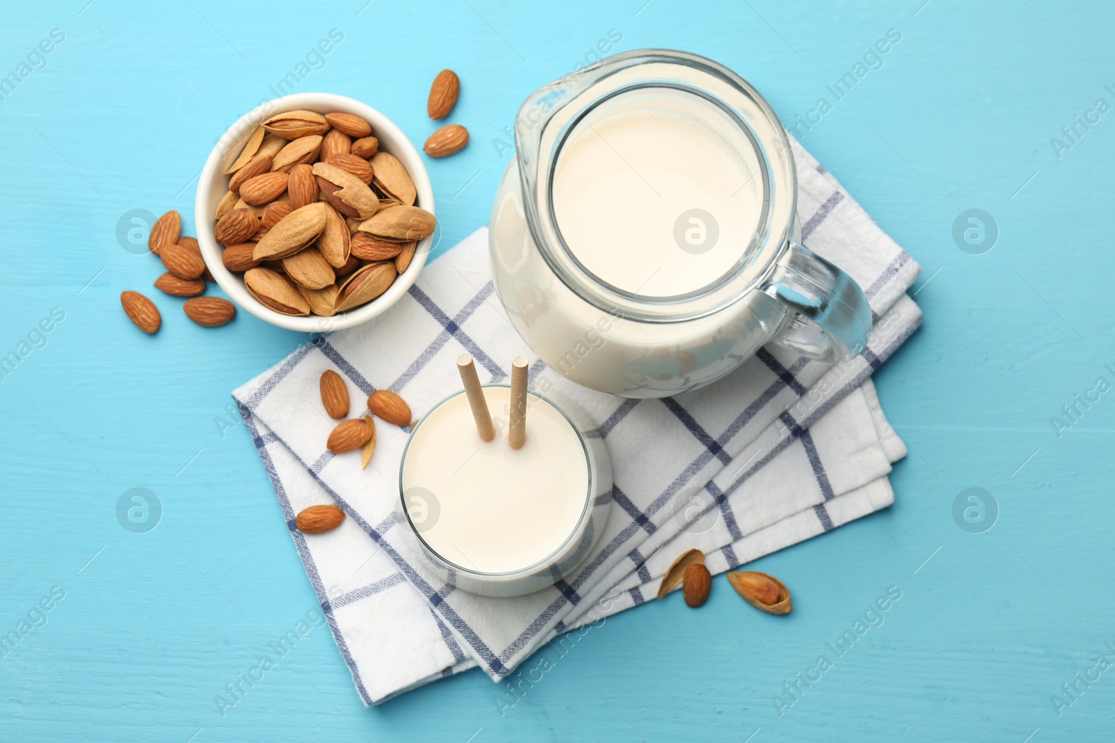 Photo of Glass of almond milk, jug and almonds on light blue wooden table, top view