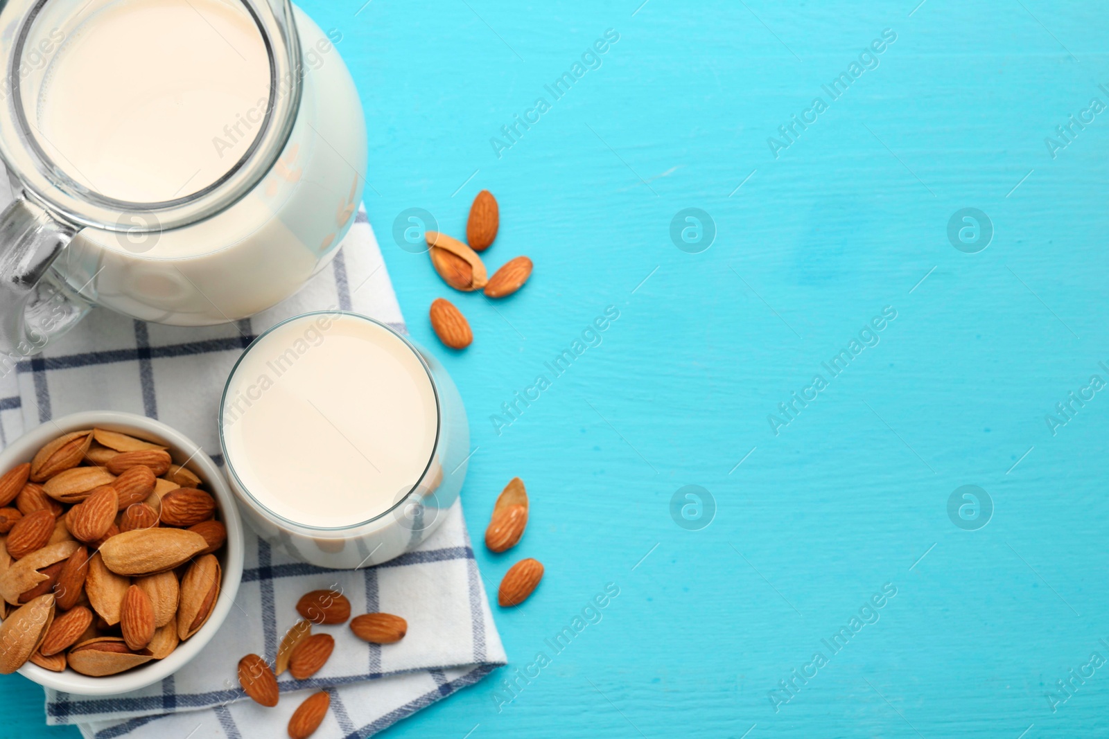 Photo of Glass of almond milk, jug and almonds on light blue wooden table, top view. Space for text