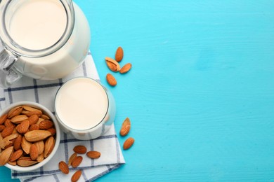 Glass of almond milk, jug and almonds on light blue wooden table, top view. Space for text