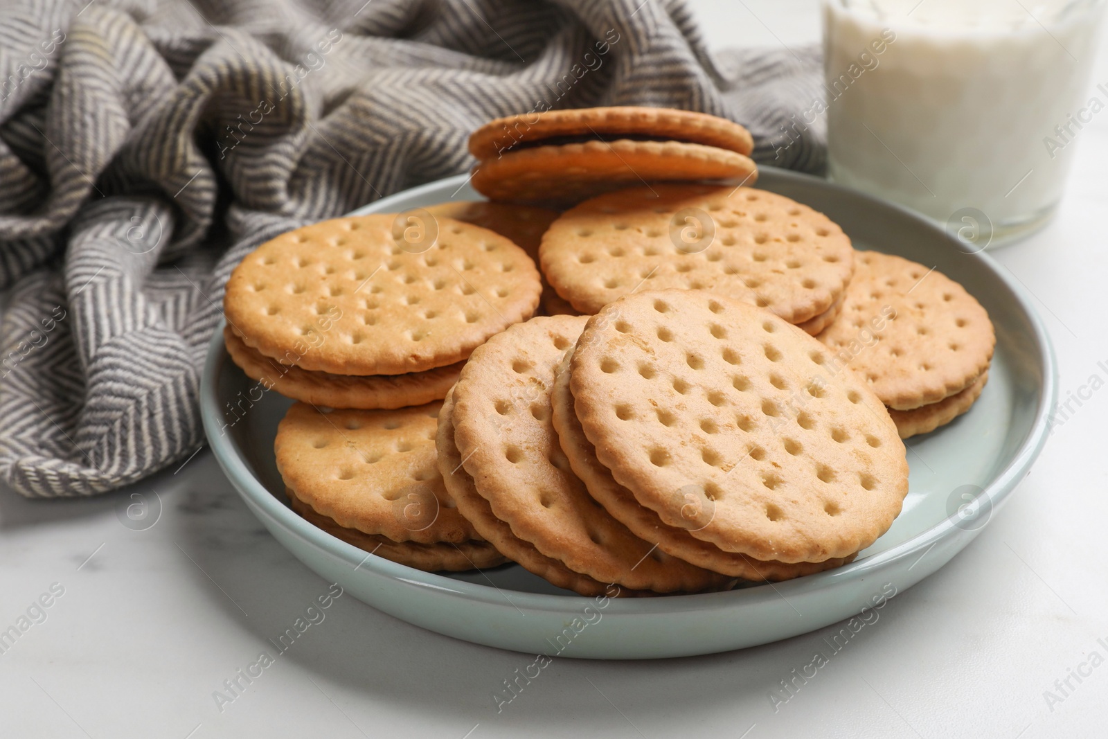 Photo of Tasty sandwich cookies and glass of milk on white table, closeup