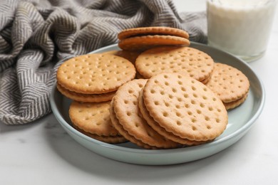 Tasty sandwich cookies and glass of milk on white table, closeup