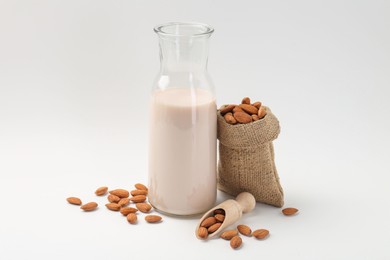 Fresh almond milk in carafe, nuts, scoop and burlap sack on white background