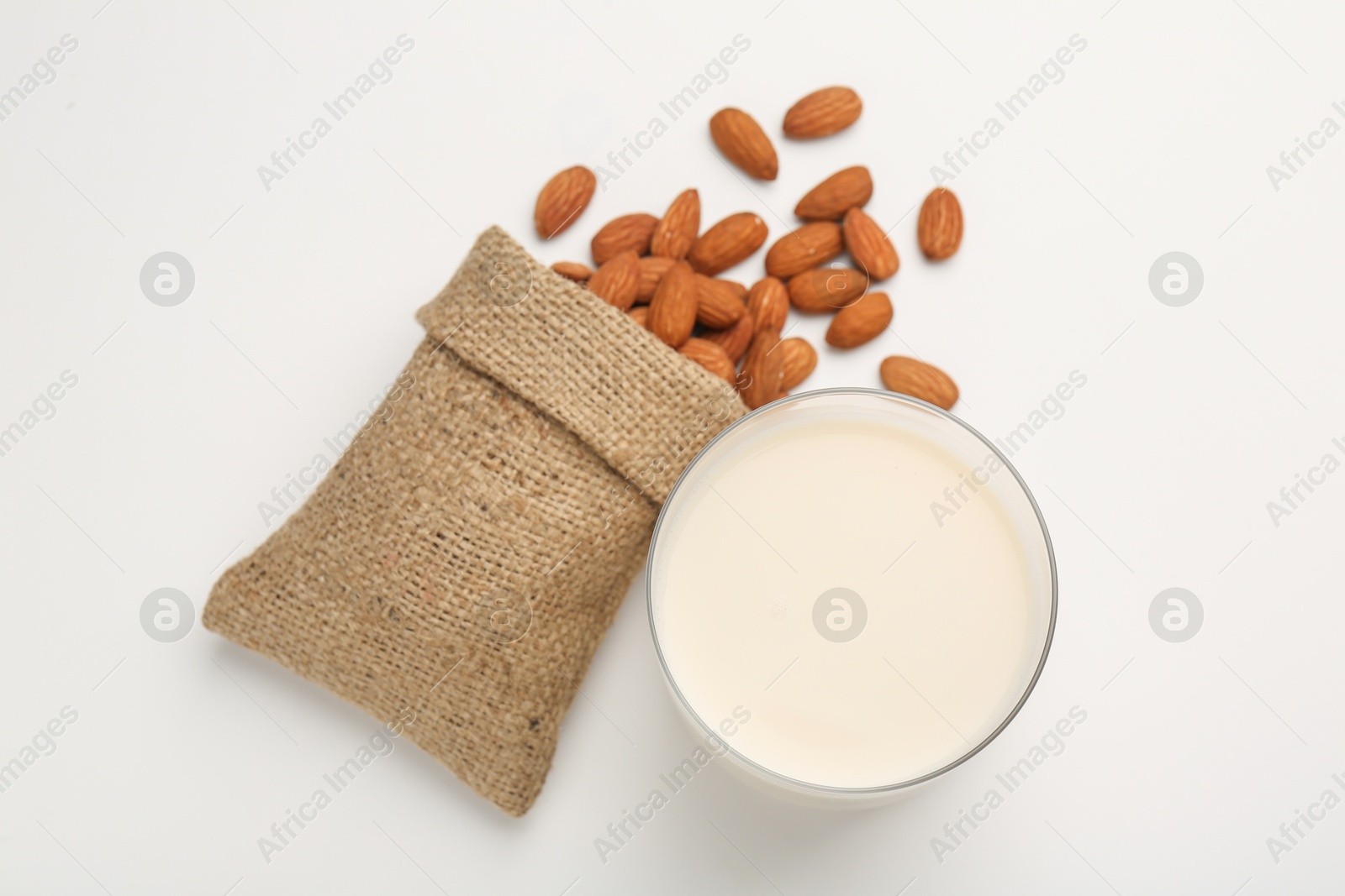 Photo of Fresh almond milk in glass, nuts and burlap sack on white background, top view