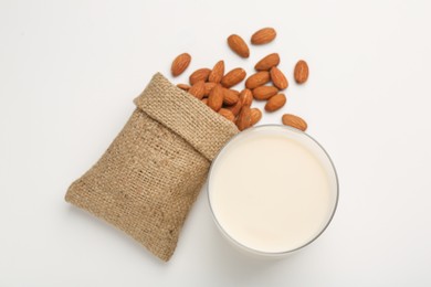 Fresh almond milk in glass, nuts and burlap sack on white background, top view