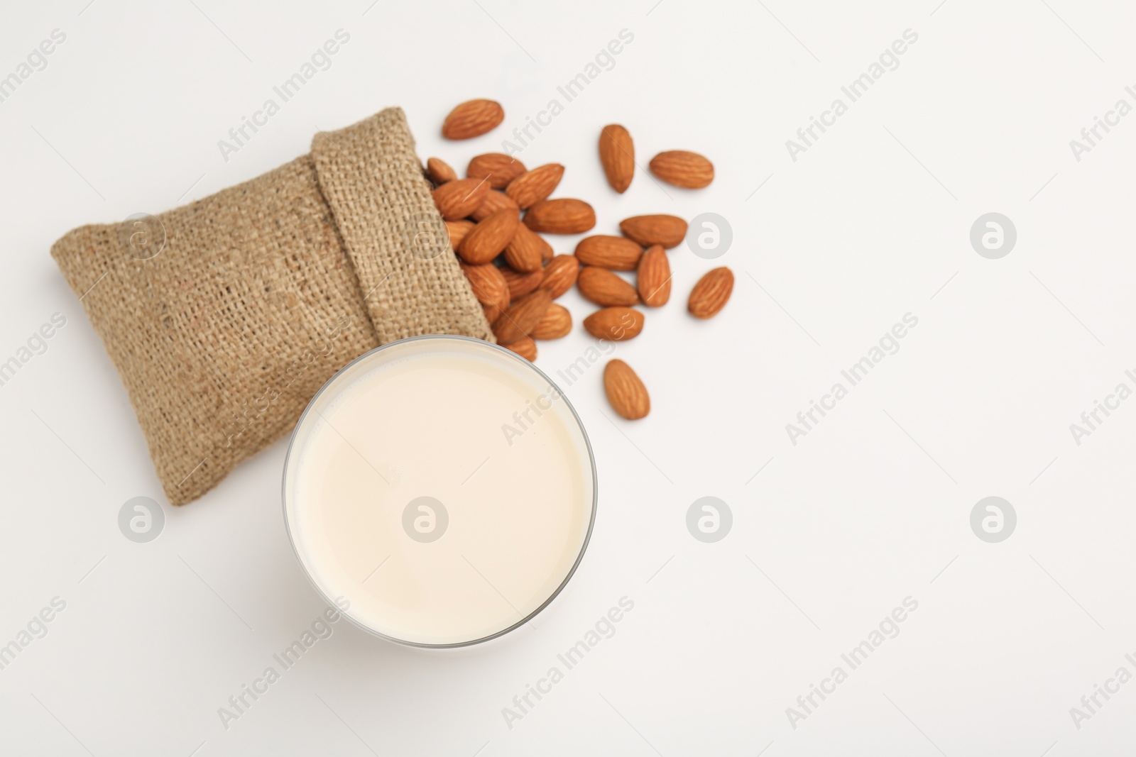 Photo of Fresh almond milk in glass, nuts and burlap sack on white background, top view. Space for text