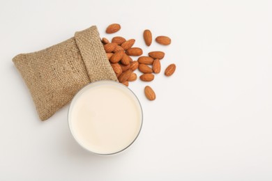 Photo of Fresh almond milk in glass, nuts and burlap sack on white background, top view. Space for text