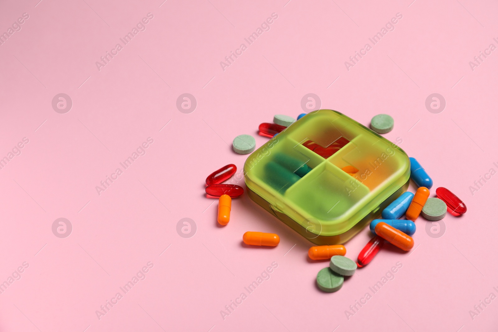 Photo of Different pills and organizer on pink background, space for text