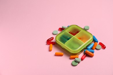 Photo of Different pills and organizer on pink background, space for text