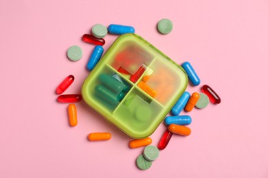 Photo of Different pills and organizer on pink background, flat lay