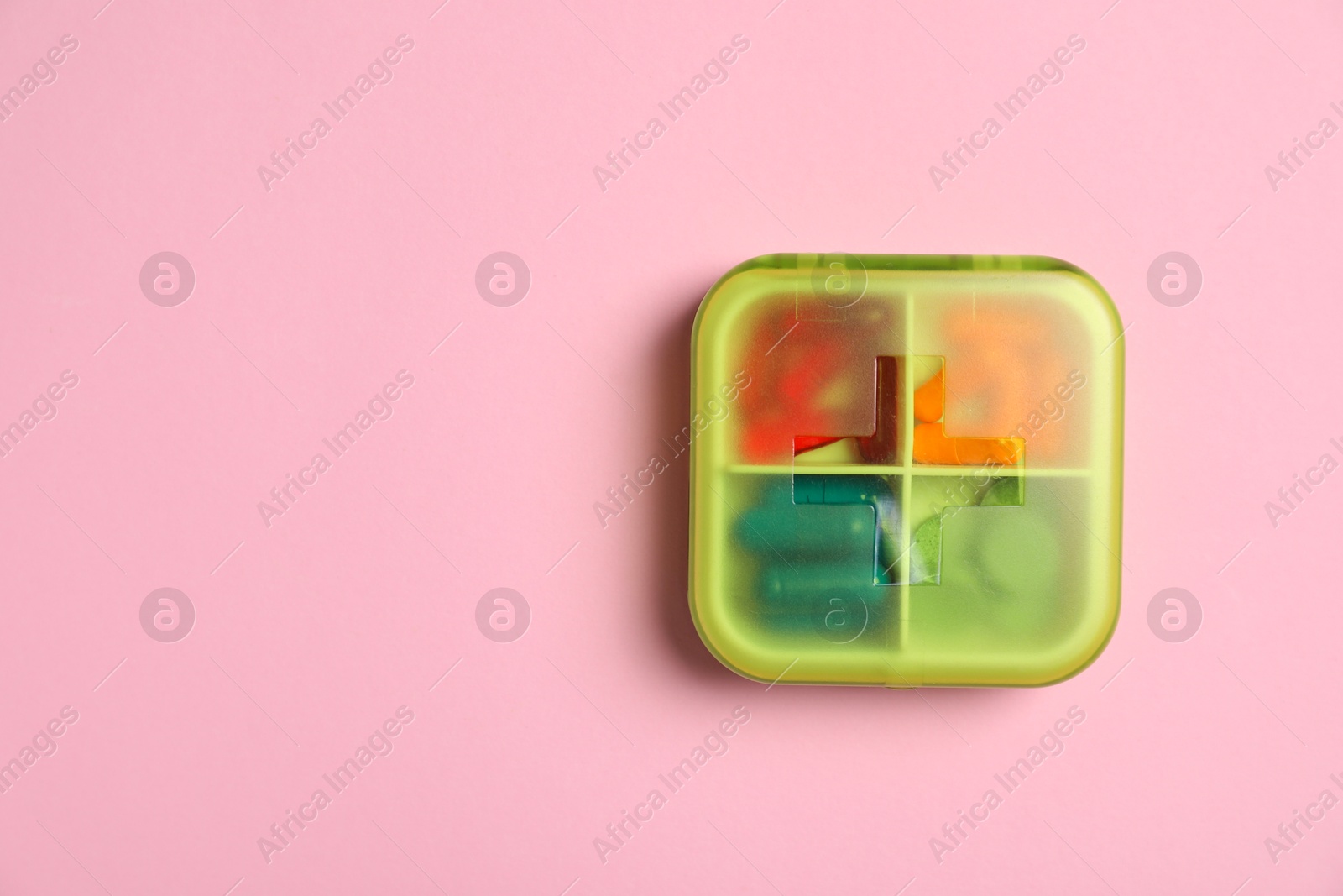 Photo of Different pills in organizer on pink background, top view. Space for text