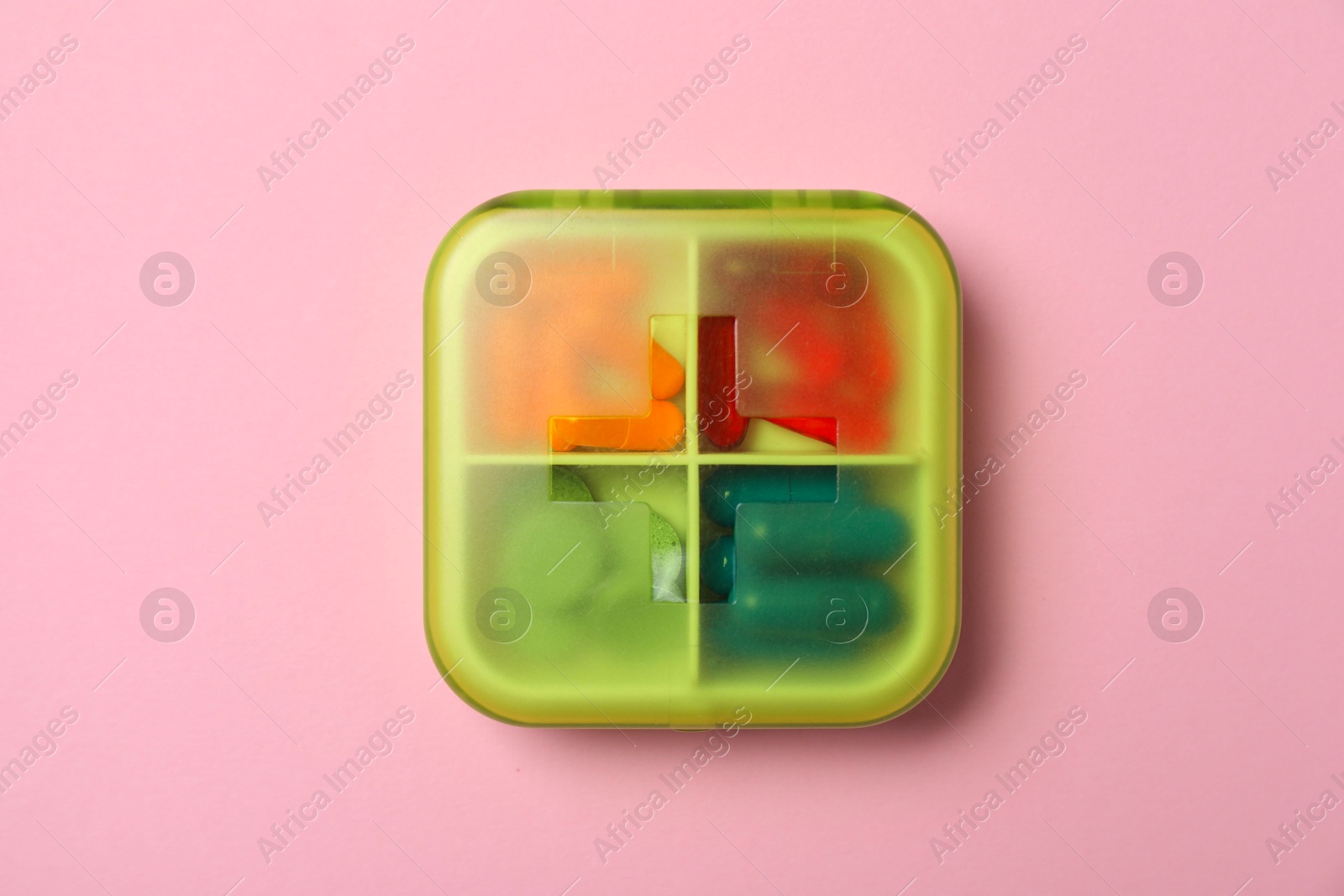 Photo of Different pills in organizer on pink background, top view