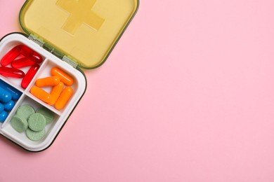 Different pills in organizer on pink background, top view. Space for text