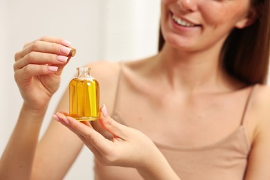 Aromatherapy. Woman with bottle of essential oil on light background, closeup