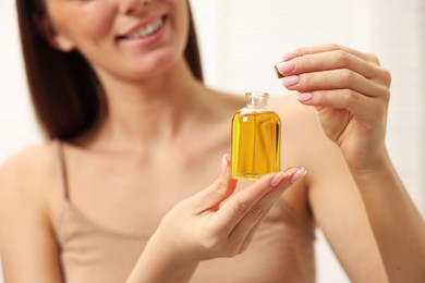 Photo of Aromatherapy. Woman with bottle of essential oil on light background, closeup