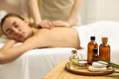 Aromatherapy. Woman receiving back massage in spa salon, focus on bottles of essential oils, burning candle and stones