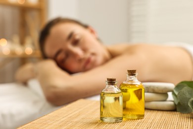 Aromatherapy. Woman relaxing on massage couch in spa salon, focus on bottles of essential oils