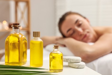 Aromatherapy. Woman relaxing on massage couch in spa salon, focus on bottles of essential oils, stones and palm leaf