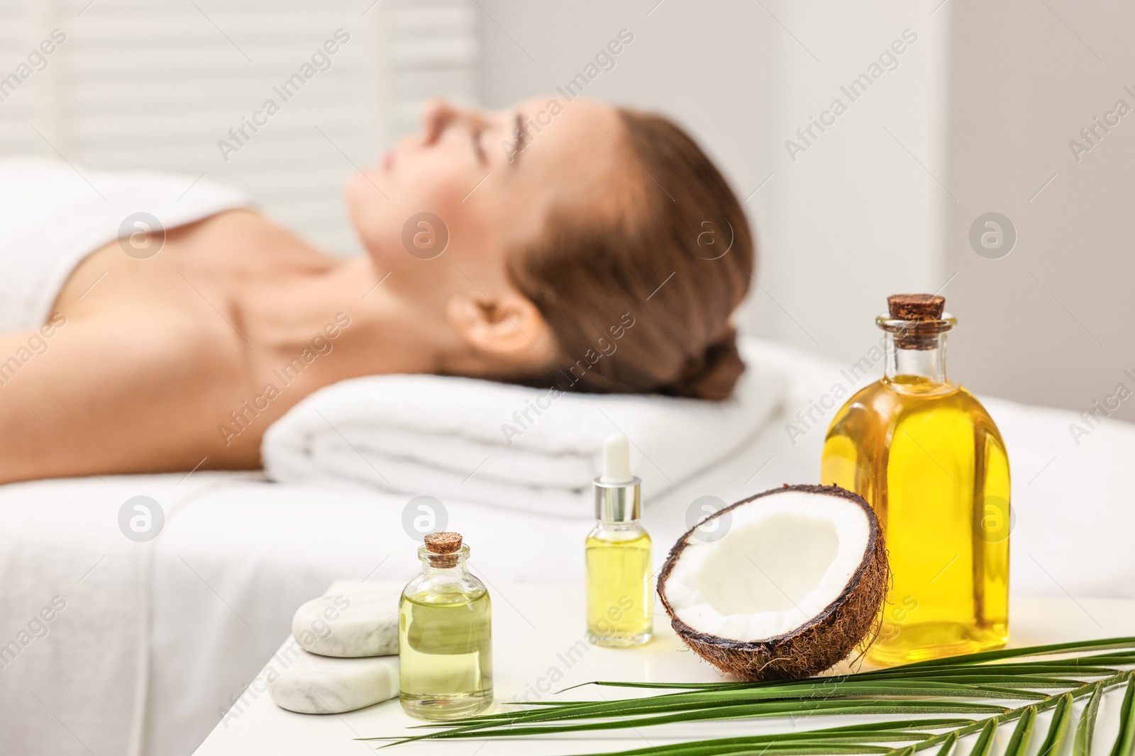 Photo of Aromatherapy. Woman relaxing on massage couch in spa salon, focus on bottles of essential oils, coconut and stones