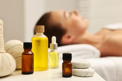 Aromatherapy. Woman relaxing on massage couch in spa salon, focus on bottles of essential oils and stones