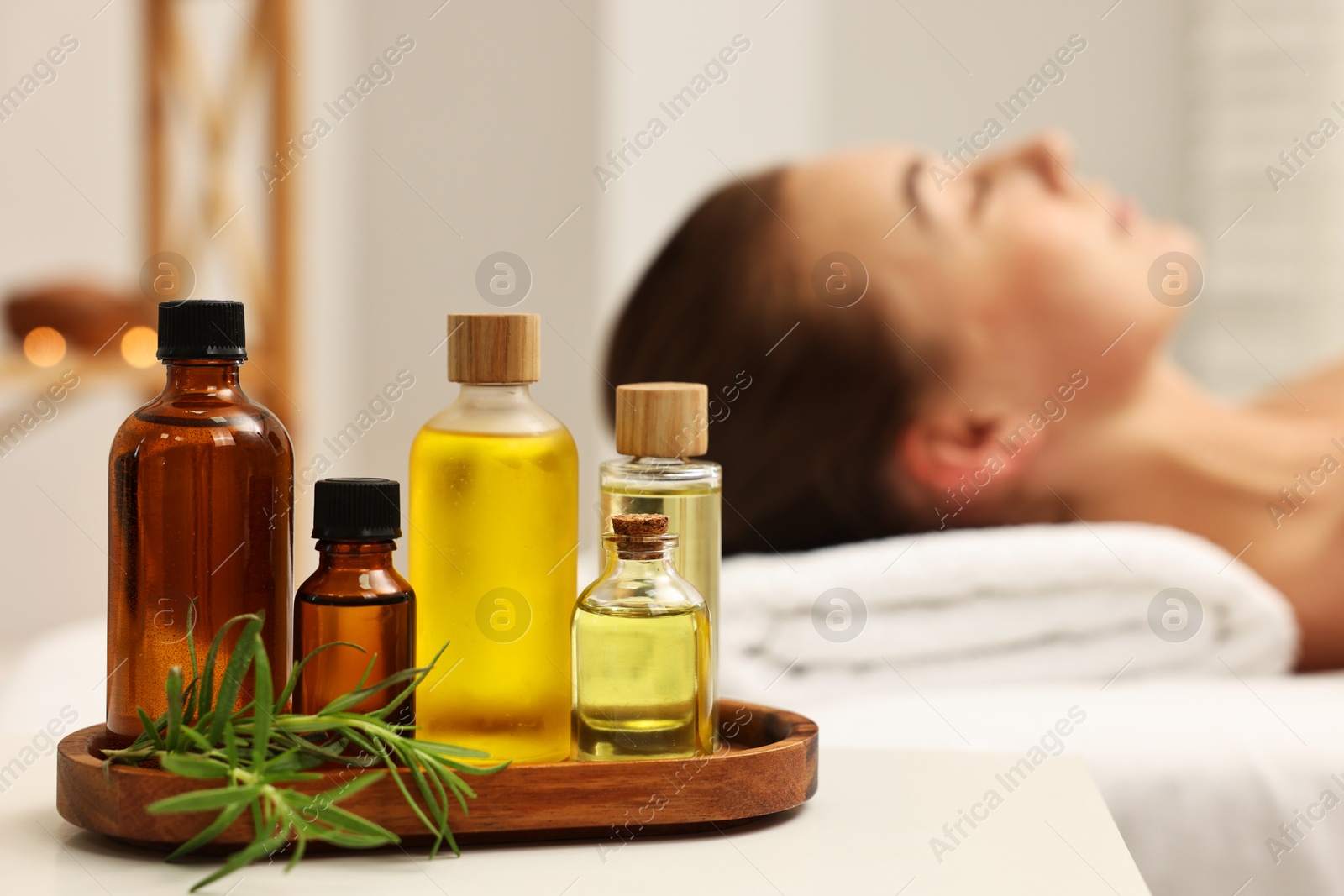 Photo of Aromatherapy. Woman relaxing on massage couch in spa salon, focus on bottles of essential oils and rosemary