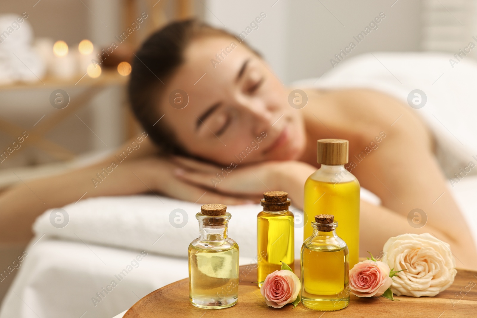 Photo of Aromatherapy. Woman relaxing on massage couch in spa salon, focus on bottles of essential oils and rose flowers